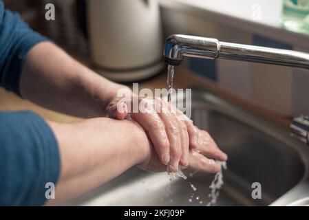 Ein Mann wäscht sich die Hände mit Seife und Wasser, während das Leitungswasser über seine Hände läuft. Stockfoto