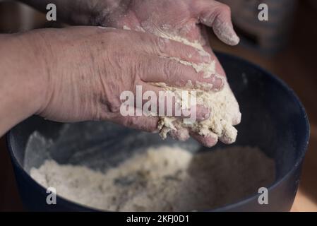 Mann, der mit den Händen Mehl und Butter in einer blauen Rührschüssel zu einer Mischung mixt. Stockfoto