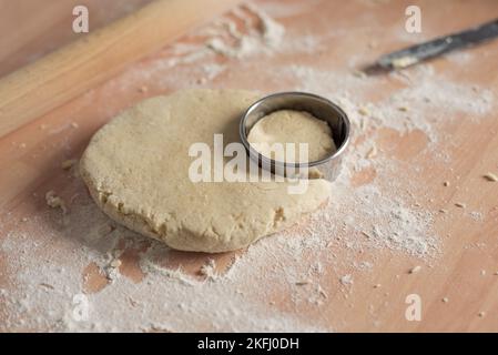 Zerkleinerer aus Metall schneidet Formen in der Scone-Mischung mit Mehl auf der Arbeitsfläche aus. Küchenutensilien. Stockfoto