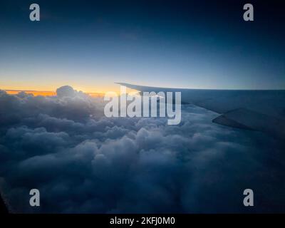 Zugeschnittenes Bild eines Flugzeugs, das während des Sonnenuntergangs über einer atemberaubenden Wolkenlandschaft fliegt Stockfoto