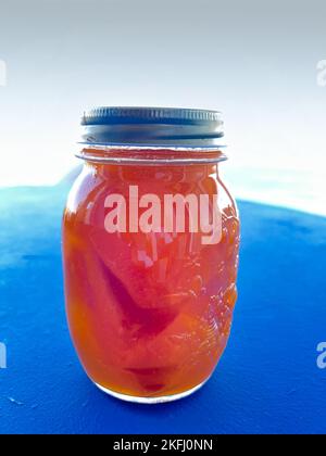 Nahaufnahme der orangefarbenen Konserven im Glasbehälter auf blauem Tisch vor weißem Hintergrund Stockfoto