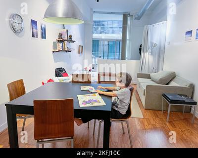 Junge mit Buntstiften, die im Buch zeichnen, während sie über einem Stuhl am Esstisch im Wohnzimmer zu Hause sitzen Stockfoto