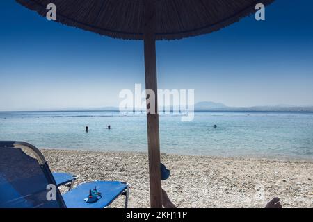 Liegestühle mit strohgedeckten Sonnenschirmen am Strand und schöner Blick auf die ruhige Meereslandschaft vor dem klaren blauen Himmel an sonnigen Tagen Stockfoto