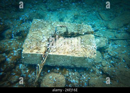 Hochwinkelansicht von Seil und Kette, die an einem Betonblock über dem Meeresboden unter blauem Meer befestigt sind Stockfoto