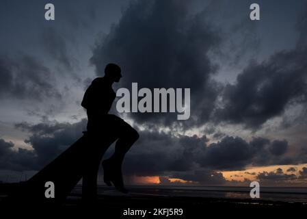 Atemberaubender Sonnenuntergang mit atemberaubenden stimmungsvollen grauen Wolken am Himmel. Halbmondskulptur in Heysham mit Metallmännern, die auf dem Gebäude sitzen und auf das Meer blicken. Stockfoto