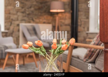 Glasvase mit orangefarbenen Tulpen. Verschwommenes Wohnzimmer. Luxuriöses Leben und Landleben. Foto aufgenommen in Rossendale am 16. November 2020. Stockfoto