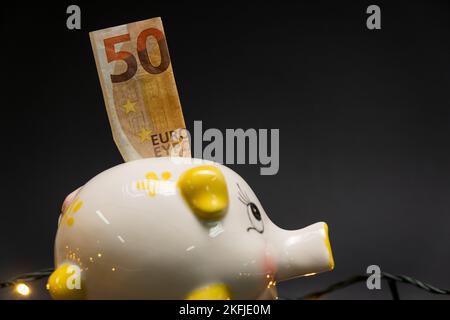 50-Euro-Banknote in einem Sparschwein, auf dunklem Hintergrund. Seitenansicht. Konzept der Kostenersparnis. Speicherplatz kopieren. Stockfoto