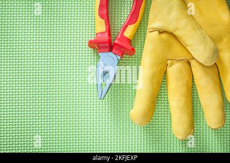 Isolationszange aus Leder mit Schutzhandschuh auf grünem Stromkonzept. Stockfoto