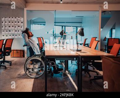 Ein Geschäftsmann mit einer Behinderung im Rollstuhl, der spät in der Nacht alleine an seinem Schreibtisch in einem Büro Überstunden machte Stockfoto