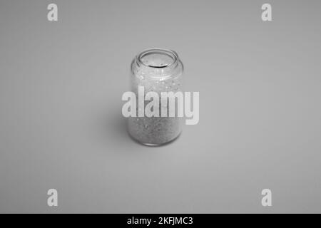 Weißes, glitzerndes Pulver in einer kleinen Glasflasche, isoliert auf grauem Hintergrund. Standleben, klassisches Einzelbild im Retro-Stil. Glitzerglas. Stockfoto