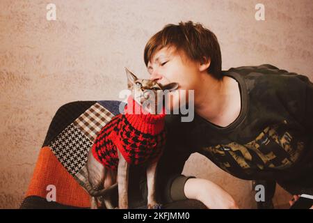 Frau küsst geliebte Katze Canadian Sphynx. Herrin und Katze in rotem Pullover. Stockfoto