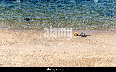 Ein Paar sitzt auf Liegen an einem großen Strand an der Nordküste Stockfoto