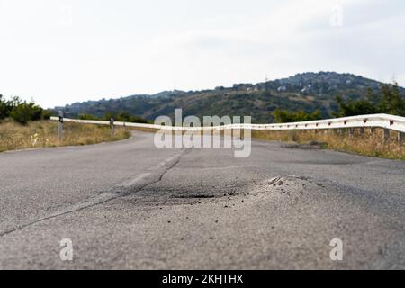 Gebrochener Fleck mitten auf einer Straße, die sich auf dem Land gegen hohe Waldberge und Hügel erstreckt Stockfoto