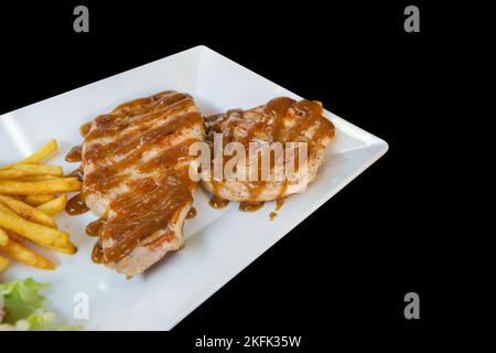 Stempelschnitt von Schweinefleisch Steak mit französisch gebraten in weißen Teller auf schwarz isoliert. Stockfoto