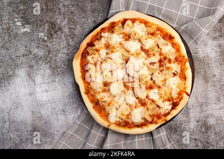 Hausgemachte Pizza mit Huhn und Ananas auf einem runden Holzschneidebrett auf dunkelgrauem Hintergrund. Draufsicht, flach liegend Stockfoto