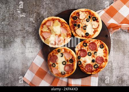 Pizzette oder Mini-Pizza auf einem runden Holzschneidebrett auf dunkelgrauem Hintergrund. Draufsicht, flach liegend Stockfoto