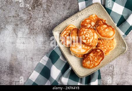 Pizzette oder Mini-Pizza auf einem runden Holzschneidebrett auf dunkelgrauem Hintergrund. Draufsicht, flach liegend Stockfoto