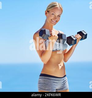 So gesund wie möglich. Porträt einer lächelnden jungen Frau, die Gewichte nach draußen hebt. Stockfoto