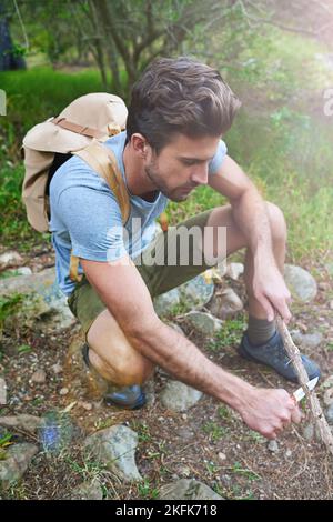 Werden Sie warm und gemütlich in der Natur. Ein gutaussehender Wanderer, der einen Ast schnitzelt. Stockfoto