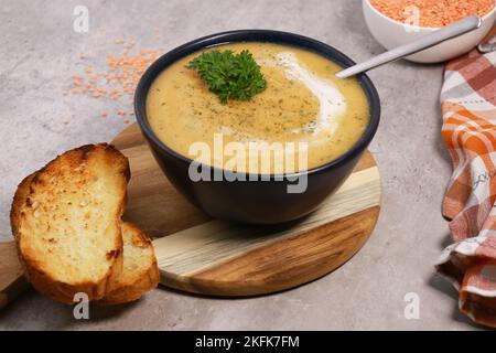 Rote Linsen Suppenpüree in dunkler Schüssel mit Brot auf grauem Marmortisch Stockfoto