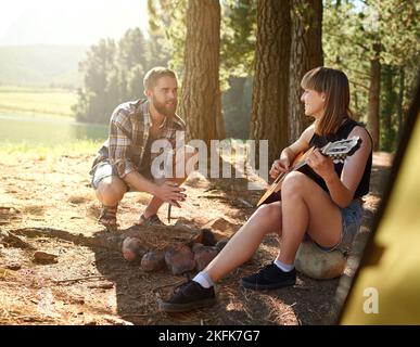 Serenading im Freien. Eine junge Frau spielt Gitarre für ihren Freund auf ihrem Campingplatz. Stockfoto