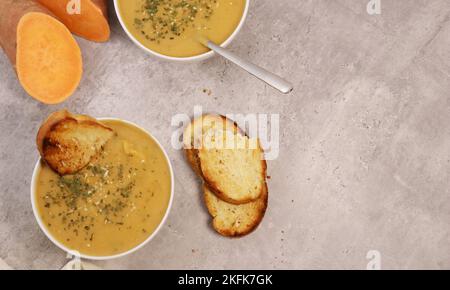 Süsskartoffelpüree-Suppe mit Knoblauchbrot auf grauem Marmortisch Stockfoto