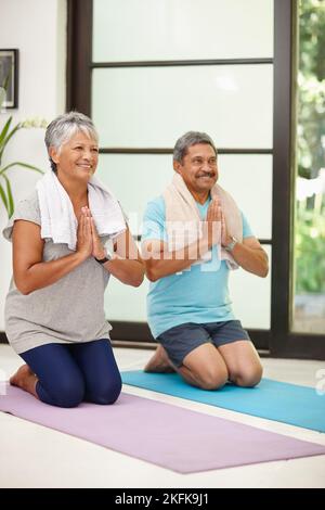 Friedlich und konzentriert. Porträt eines reifen Paares, das zu Hause gemeinsam Yoga macht. Stockfoto