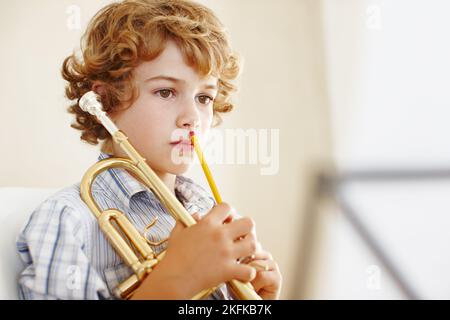 Übung hält ihn diszipliniert. Ein süßer kleiner Junge spielt Trompete. Stockfoto