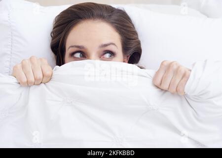 In der Nacht wurde etwas angestoßen... Eine junge Frau, die mit einem verängstigten Gesichtsausdruck aus ihrem NED-Laken herausguckte. Stockfoto