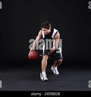 Er spielt, um zu gewinnen. Ganzkörperaufnahme eines männlichen Basketballspielers in Aktion vor schwarzem Hintergrund. Stockfoto