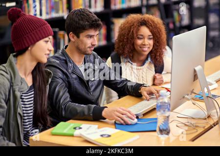 Eine Gruppe von Studenten, die an einem Computer in einer Universitätsbibliothek zusammenarbeiten. Stockfoto