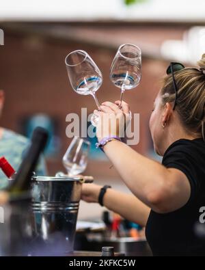 Eine vertikale Aufnahme einer Kellnerin, die zwei Weingläser in ihren Händen auf einem isolierten Hintergrund hält Stockfoto