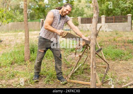 Glücklicher Holzfäller, der Holz im Garten sägt Stockfoto