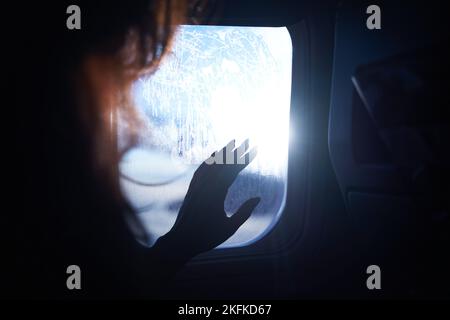 Weibliche Hand berührt die warmen Sonnenstrahlen vom Flugzeugfenster. Frau freut sich auf die Reise in ihren Urlaub. Mädchen auf einer Reise Flug sitzen in Stockfoto