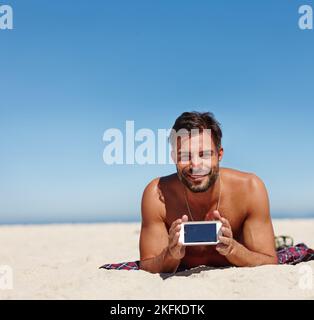 Dieser Weg in Ihren Urlaub. Ein junger Mann zeigt einen leeren Handy-Bildschirm, während am Strand. Stockfoto