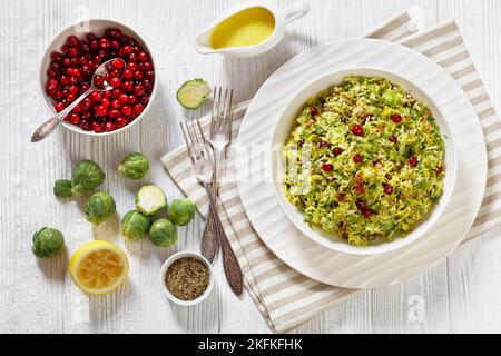 rosenkohl mit Mandeln, knusprig gebratenem Speck und Preiselbeeren in weißer Schale auf Holztisch mit Zutaten, horizontale Ansicht von oben, fl Stockfoto