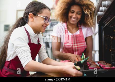 Mutter und Tochter nehmen Muffins aus dem Ofen in der Küche, Erwachsene Frau und junges Mädchen backen Cupcakes, Quarantäne, Wochenende, Bonding Aktivitäten conce Stockfoto