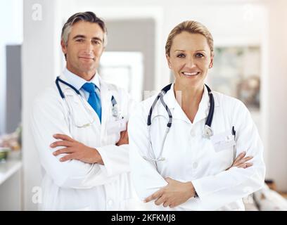 Lassen Sie Ihre Gesundheit in unseren sicheren Händen. Beschnittenes Porträt von zwei Ärzten, die mit gekreuzten Armen im Krankenhausflur stehen. Stockfoto