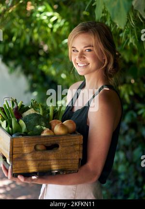 Nichts schmeckt so gut wie hausgemachten Gemüse. Eine junge Frau, die eine Kiste mit Gemüse im Freien hält. Stockfoto