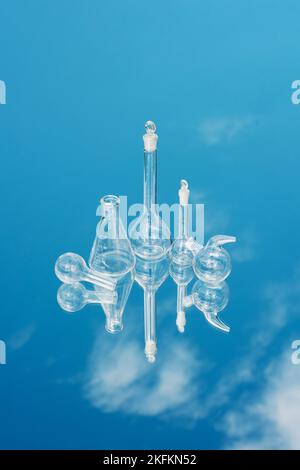 Verschiedene Laborglaswaren auf einem spiegelnden Hintergrund mit Himmelsreflexion. Wissenschaftliche Laborforschung und -Entwicklung Labor- und Entwicklungskonzept Stockfoto