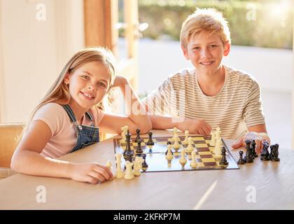 Portrait, Schach und Kinder entspannen sich an einem Tisch mit Brettspiel, Bindung und Lernen in einem Wohnzimmer in ihrem Zuhause. Kinder, Schachbrett und Gehirnaktivität Stockfoto