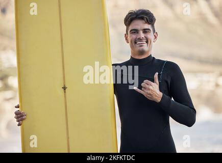 Fröhlicher Surfer, Handzeichen und Mann, Portrait und Motivation, Strand- und Sommersport, Freiheit und Glück bei Sonnenschein. Surfbrett, shaka und Smile Stockfoto