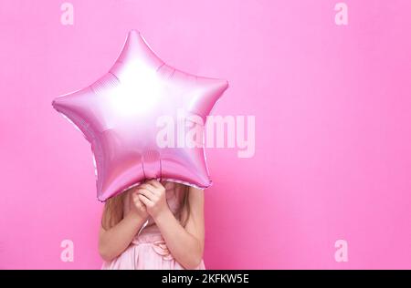 Ein unbekanntes Mädchen steht und hält einen Ballon in der Form eines Sterns, der ihr Gesicht bedeckt. Das Konzept eines Urlaubs mit Luftballons mit Platz zum Kopieren. Hochwertige Fotos Stockfoto