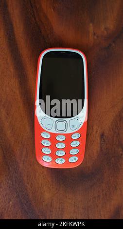 Ein Telefon mit Tastenfeld, dessen Tasten auf schwarzem Hintergrund isoliert sind. Altes Mobiltelefon mit schwarzem Display. Nahaufnahme eines orangefarbenen Mobils von 2g, 3G in Indien. Technologie und Stockfoto