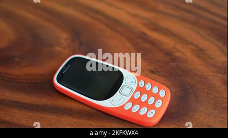 Ein Telefon mit Tastenfeld, dessen Tasten auf schwarzem Hintergrund isoliert sind. Altes Mobiltelefon mit schwarzem Display. Nahaufnahme eines orangefarbenen Mobils von 2g, 3G in Indien. Technologie und Stockfoto