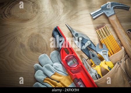 Sortiment von Bauwerkzeugen in Leder-Baugurt auf Holzbrett. Stockfoto