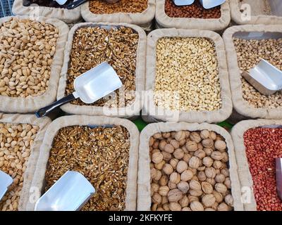 Verschiedene Arten von Nüssen viel in Landwirt Shop. Draufsicht. Natürliche Walnüsse, Cashewkerne, Pistazien, Erdnüsse, Haselnüsse, Pfirsichgruben. Stockfoto