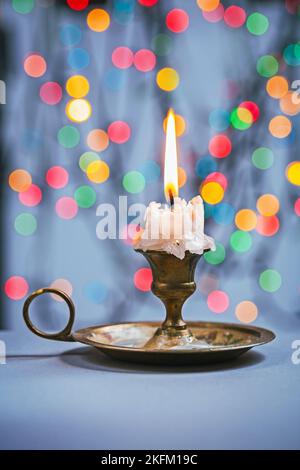 Nahaufnahme der Kerze im Kerzenständer auf dem blauen Tisch und Hintergrund des Bokeh Stockfoto