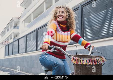 Glückliche Frau im mittleren Alter, die in der Stadt mit einem bunten Pullover Fahrrad fährt. Grüner Transport-Modus und Outdoor-städtischen Freizeitaktivitäten mit Pretty Stockfoto