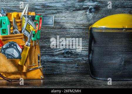 Bauwerkzeuge in Werkzeuggürtel und Sicherheitsmaske auf Vintage-Holz Stockfoto